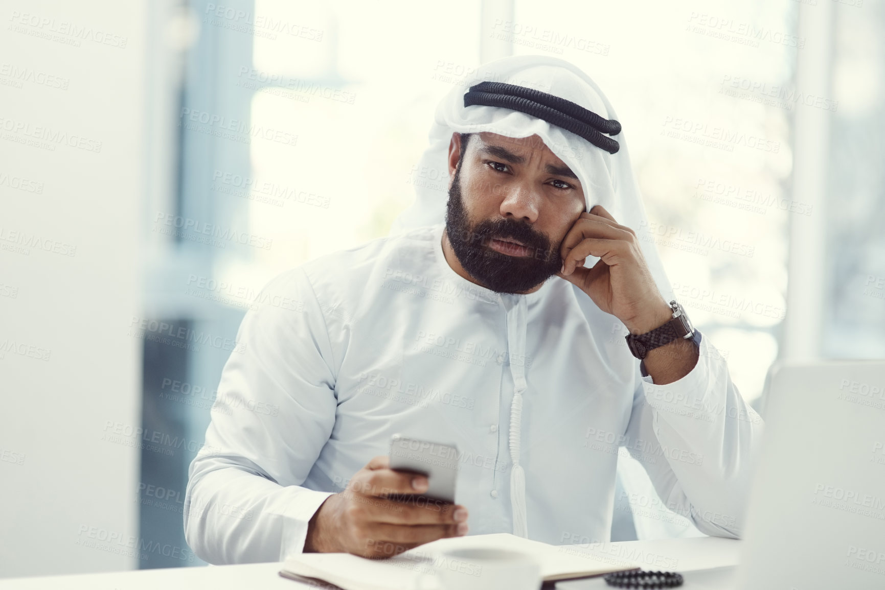 Buy stock photo Cropped portrait of a young businessman dressed in Islamic traditional clothing using his cellphone while working in his office