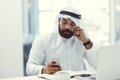 Buy stock photo Cropped shot of a young businessman dressed in Islamic traditional clothing using his cellphone while working in his office