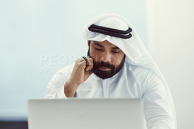 Buy stock photo Cropped shot of a young businessman dressed in Islamic traditional clothing holding prayer beads while working in his office