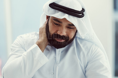 Buy stock photo Cropped shot of a young businessman dressed in Islamic traditional clothing rubbing his neck while working in his office