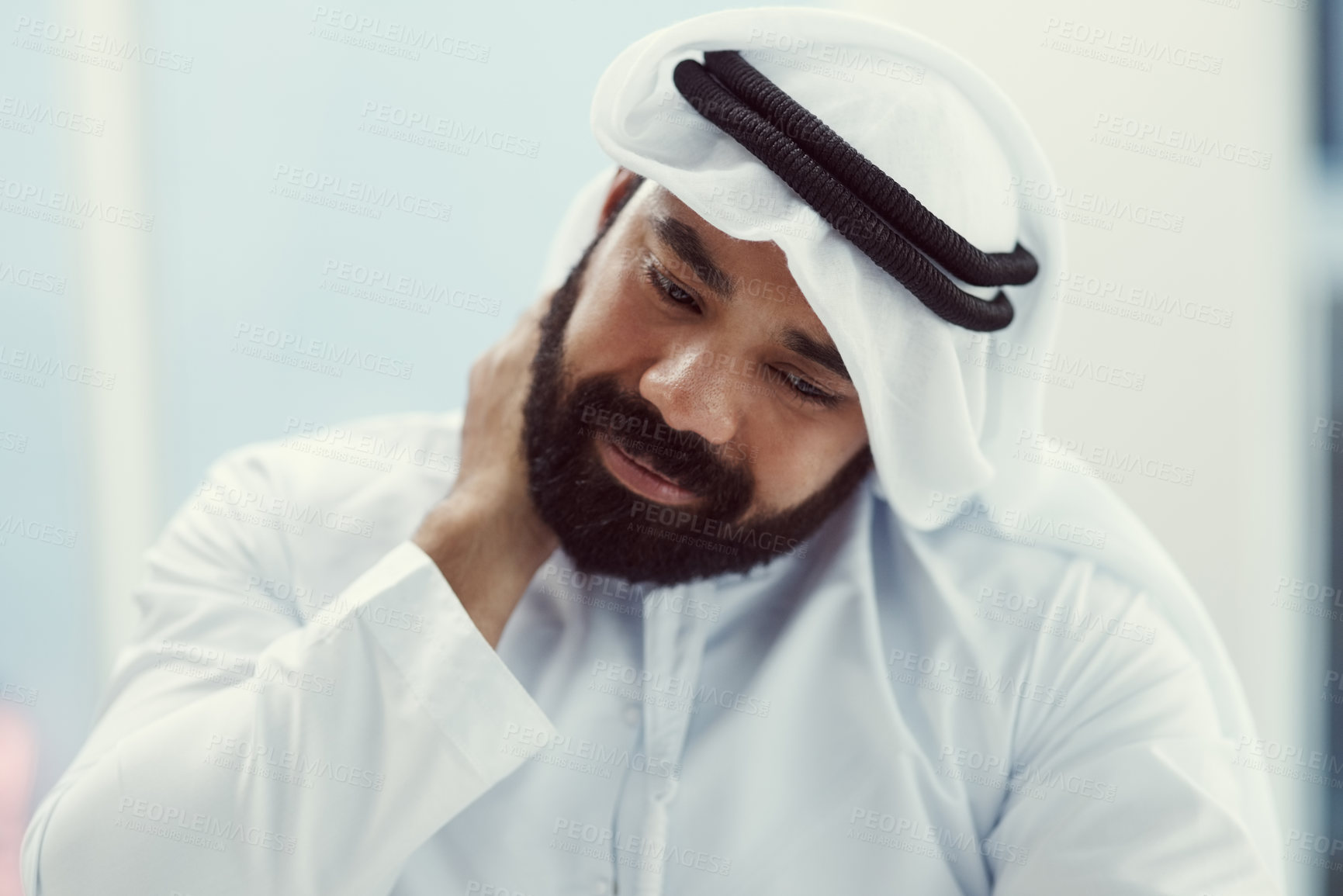 Buy stock photo Cropped shot of a young businessman dressed in Islamic traditional clothing rubbing his neck while working in his office