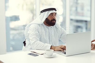 Buy stock photo Cropped shot of a young businessman dressed in Islamic traditional clothing working on his laptop while sitting in the office