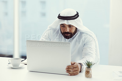 Buy stock photo Cropped shot of a young businessman dressed in Islamic traditional clothing working on his laptop while sitting in the office