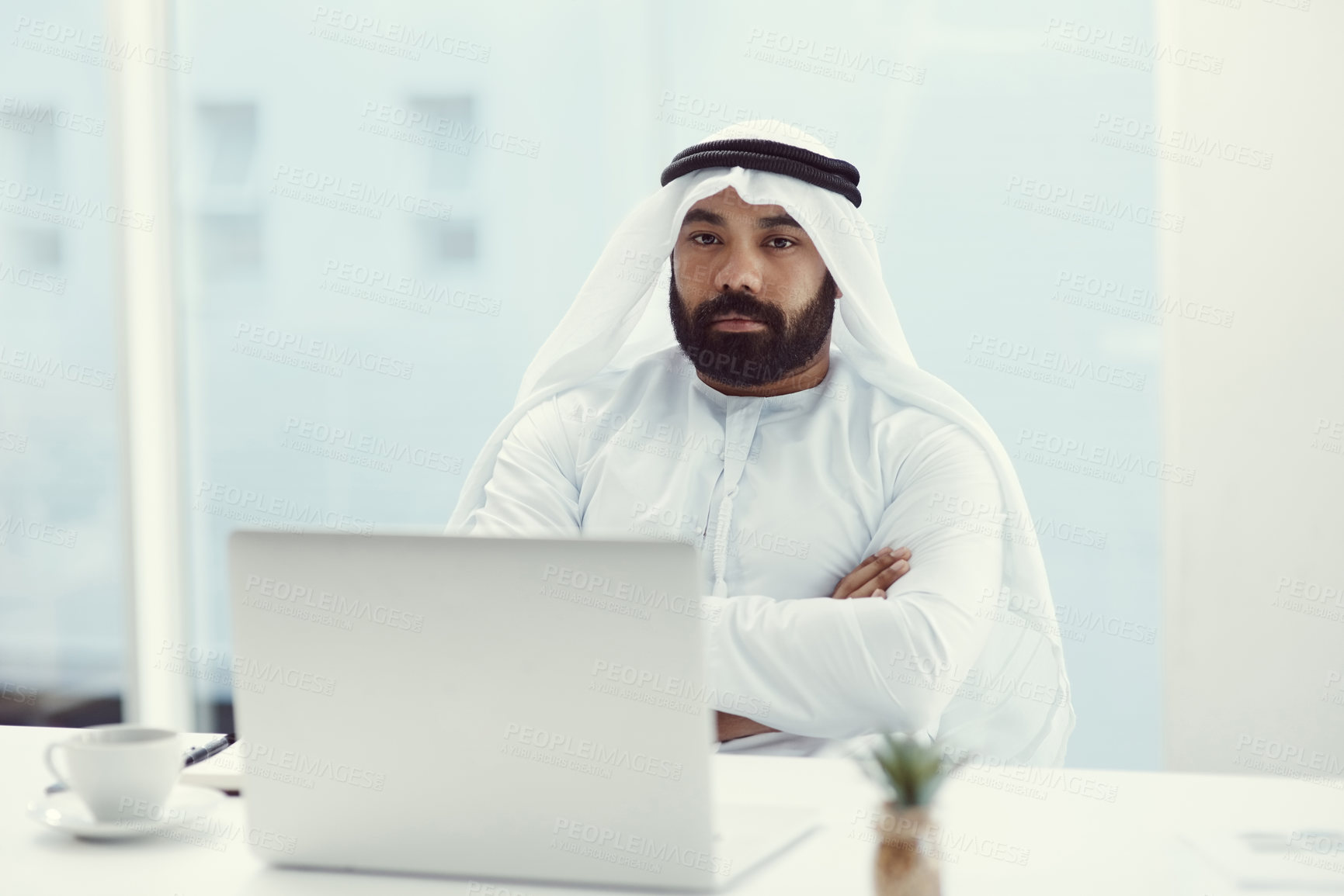 Buy stock photo Cropped portrait of a young businessman dressed in Islamic traditional clothing sitting with his arms folded in the office