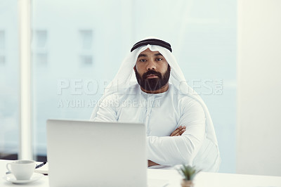 Buy stock photo Cropped portrait of a young businessman dressed in Islamic traditional clothing sitting with his arms folded in the office