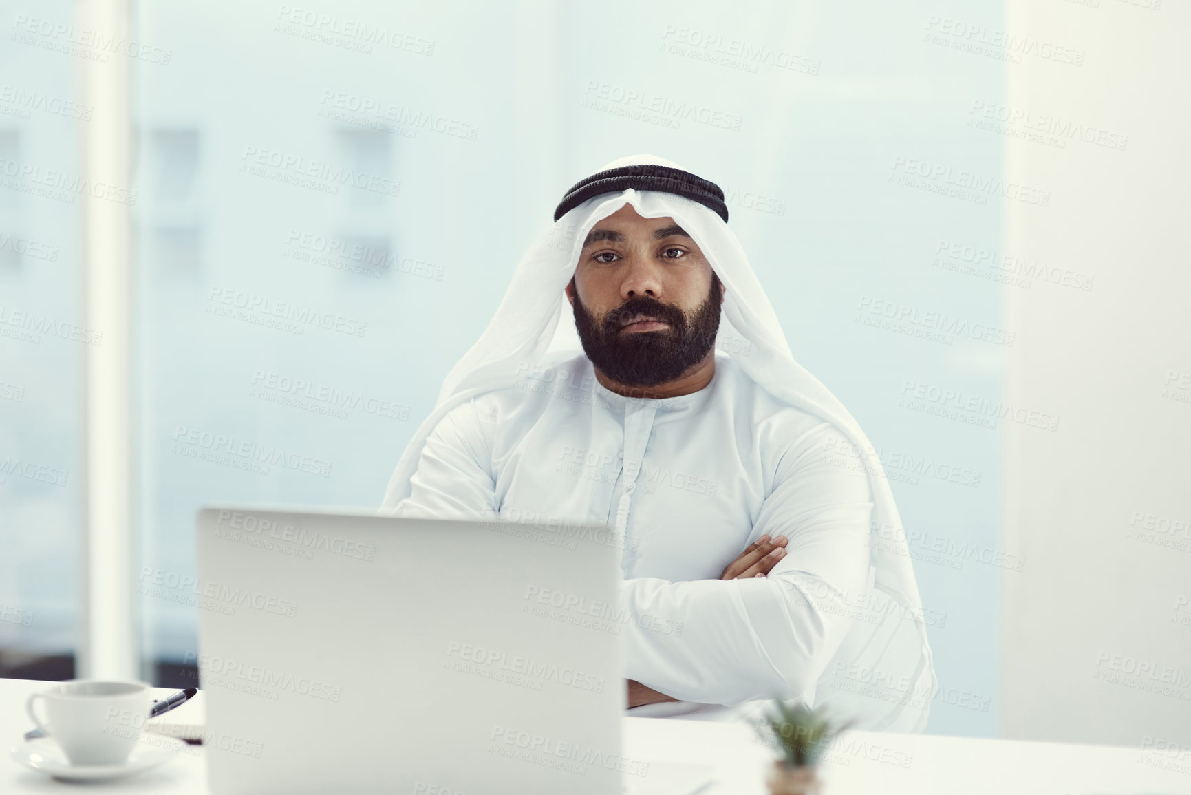 Buy stock photo Cropped portrait of a young businessman dressed in Islamic traditional clothing sitting with his arms folded in the office