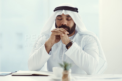 Buy stock photo Cropped shot of a young businessman dressed in Islamic traditional clothing praying while working in his office