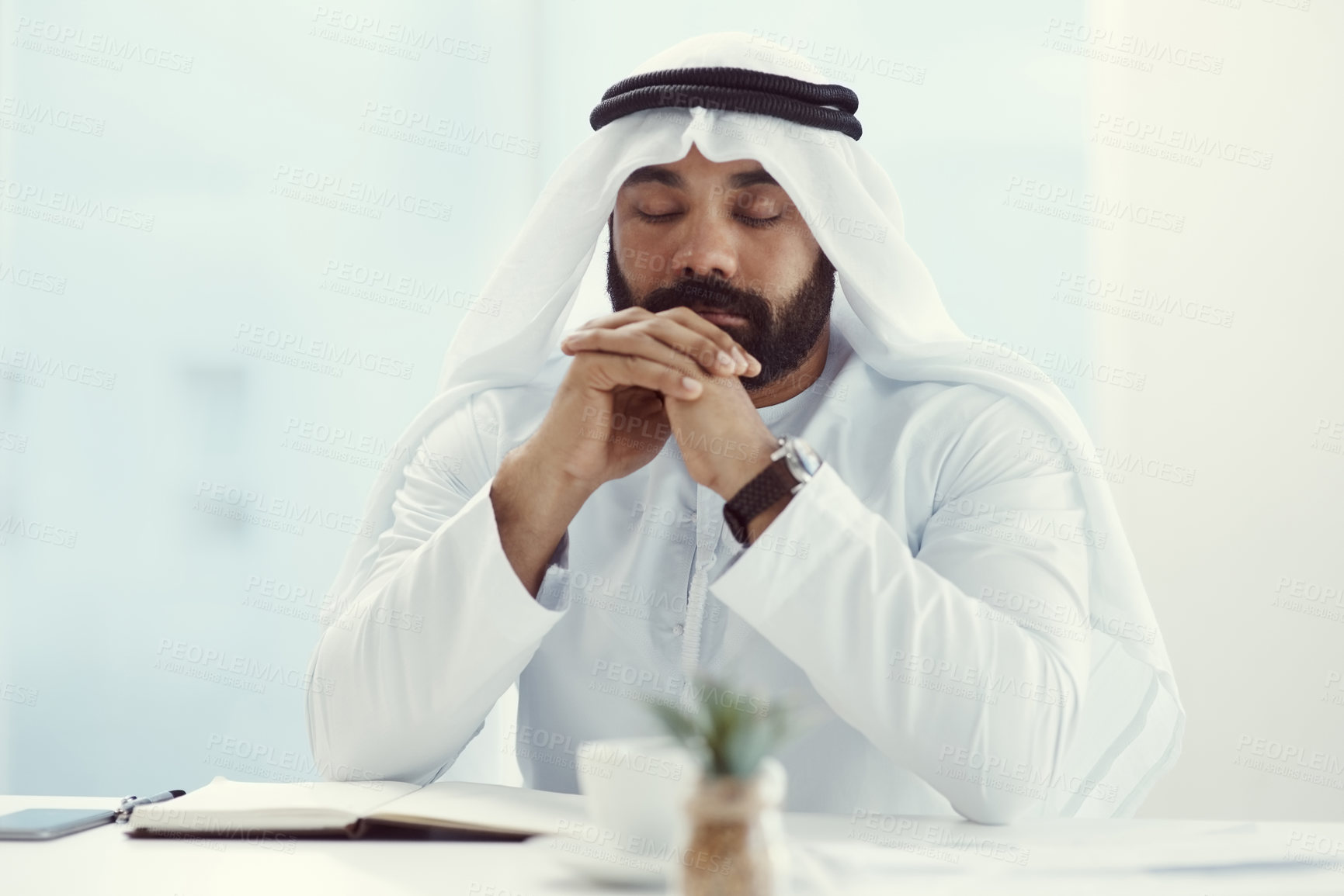 Buy stock photo Cropped shot of a young businessman dressed in Islamic traditional clothing praying while working in his office