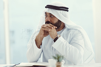 Buy stock photo Cropped shot of a young businessman dressed in Islamic traditional clothing looking thoughtful while sitting in his office