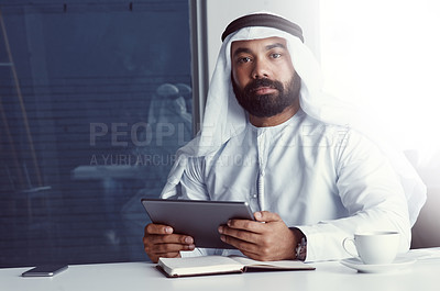 Buy stock photo Cropped portrait of a young businessman dressed in Islamic traditional clothing using a digital tablet while working in his office