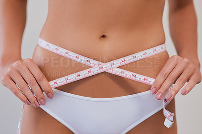 Buy stock photo Studio shot of an unrecognizable woman taking measurements of her waist against a grey background