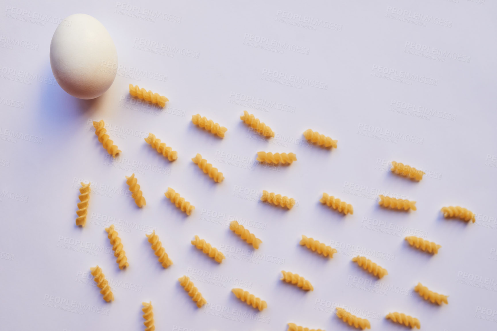 Buy stock photo Studio shot of an egg against a grey background while being surrounded by lots of little pieces of pasta