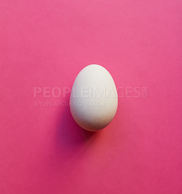 Buy stock photo Studio shot of a white egg placed in the centre against a pink background