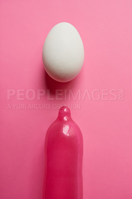 Buy stock photo Studio shot of a pink condom and a egg placed against a pink background