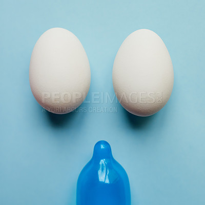 Buy stock photo Studio shot of a blue condom and two eggs placed against a blue background