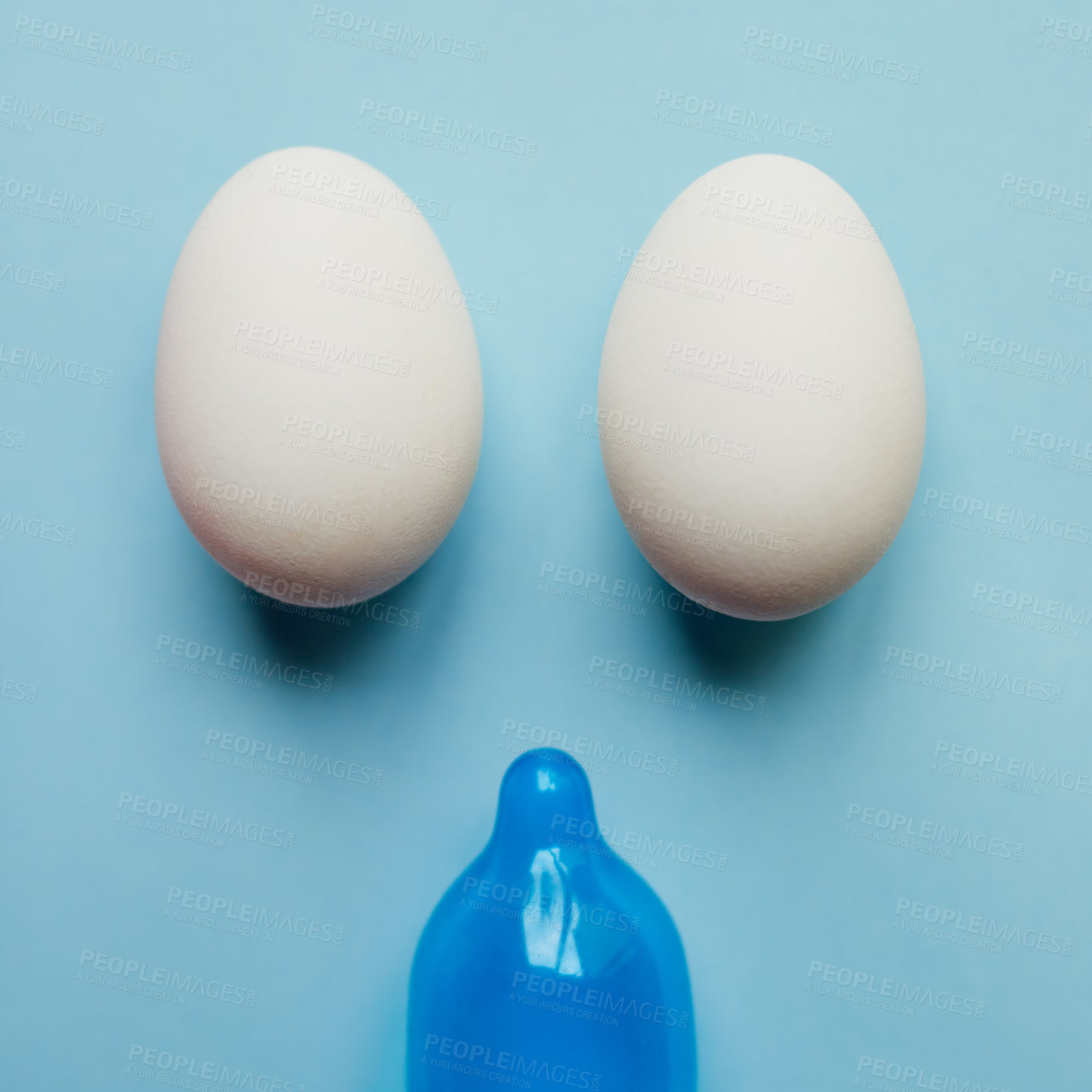 Buy stock photo Studio shot of a blue condom and two eggs placed against a blue background