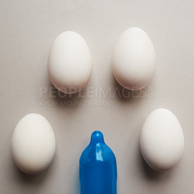 Buy stock photo Studio shot of a blue condom and four eggs placed against a grey background