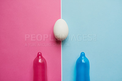 Buy stock photo Studio shot of a pink and blue condom  placed next to an egg against a pink and blue background