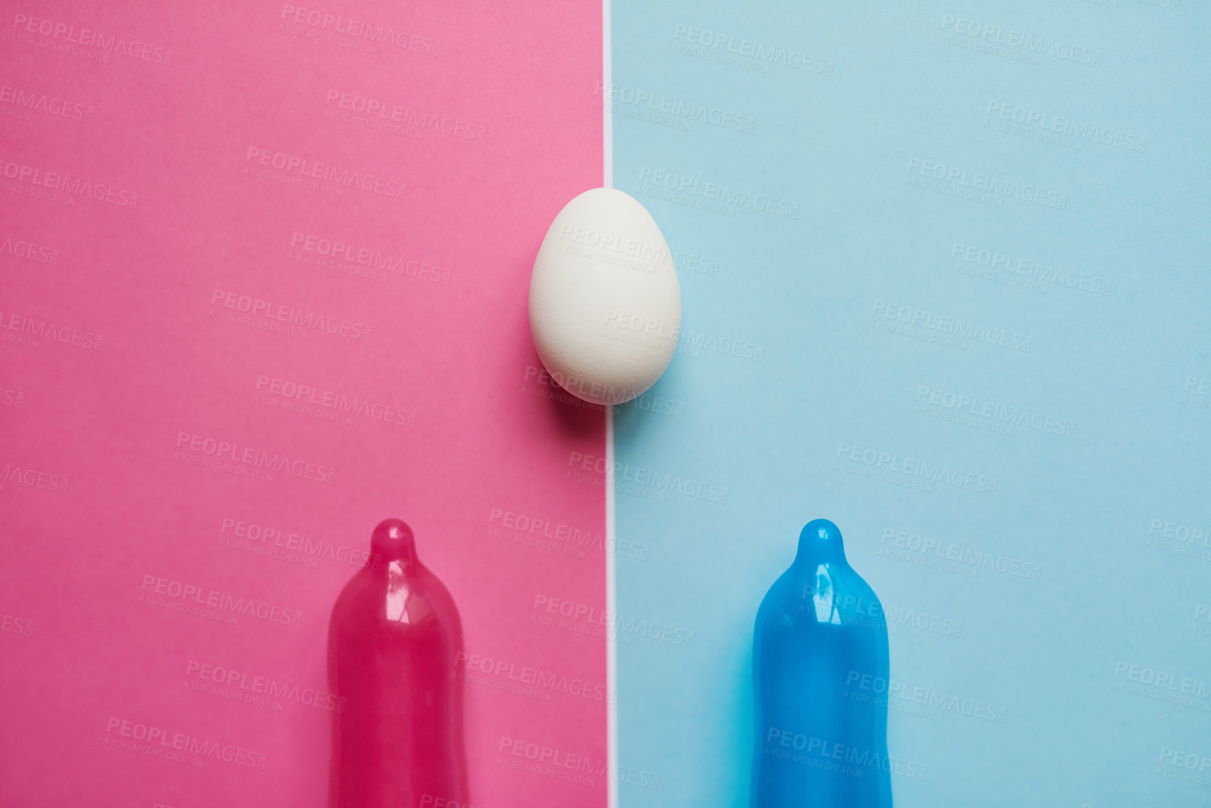 Buy stock photo Studio shot of a pink and blue condom  placed next to an egg against a pink and blue background