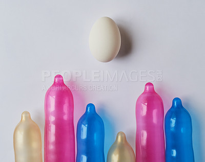Buy stock photo Studio shot of a bunch of different size and colored condoms placed next to each other with one egg on the top