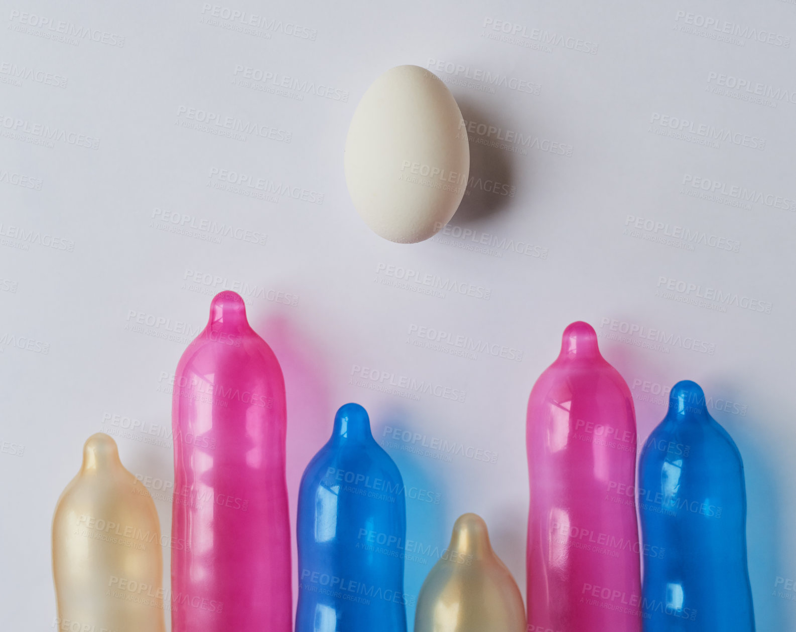 Buy stock photo Studio shot of a bunch of different size and colored condoms placed next to each other with one egg on the top