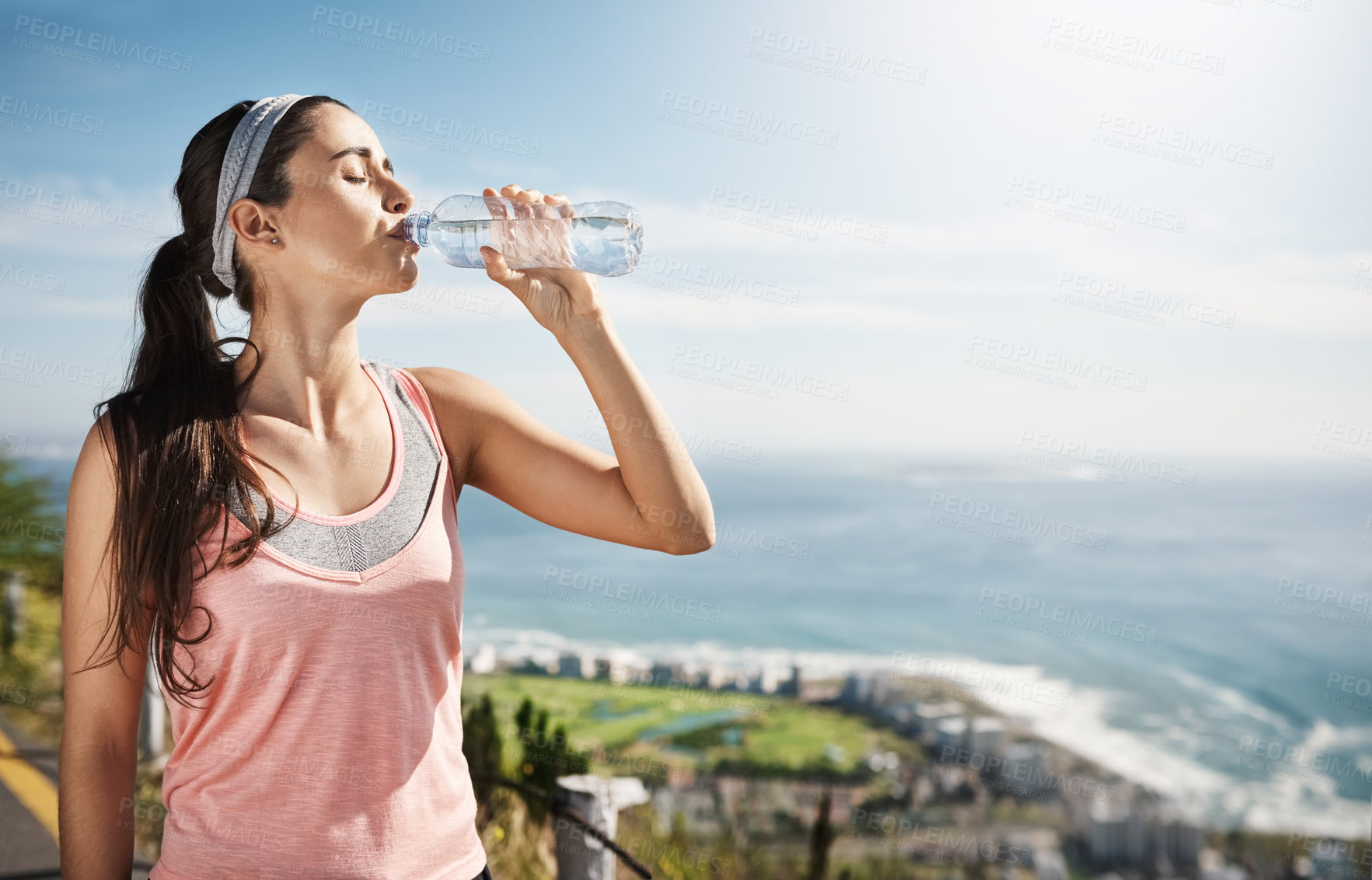 Buy stock photo Cropped shot of a young woman drinking a bottle of water while out exercising