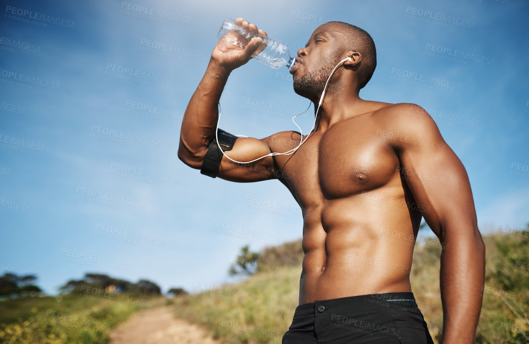 Buy stock photo Cropped shot of a young man drinking a bottle of water while out exercising