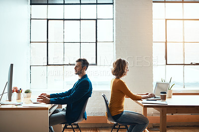 Buy stock photo Cropped shot of two young businesspeople working back to back in a modern office