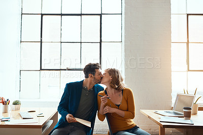 Buy stock photo Cropped shot of young couple kissing while working together in their modern office