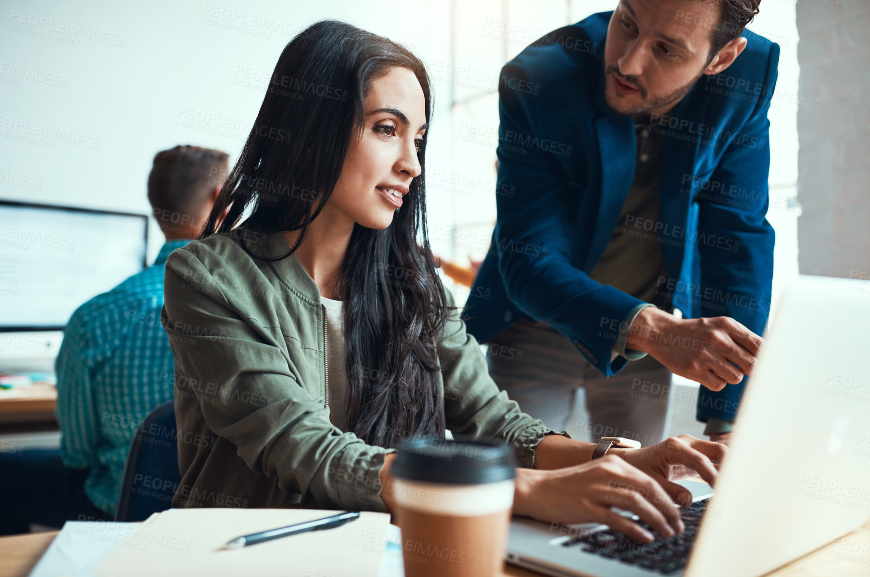 Buy stock photo Shot of two young business colleagues working together in their modern office with a male colleague in the background