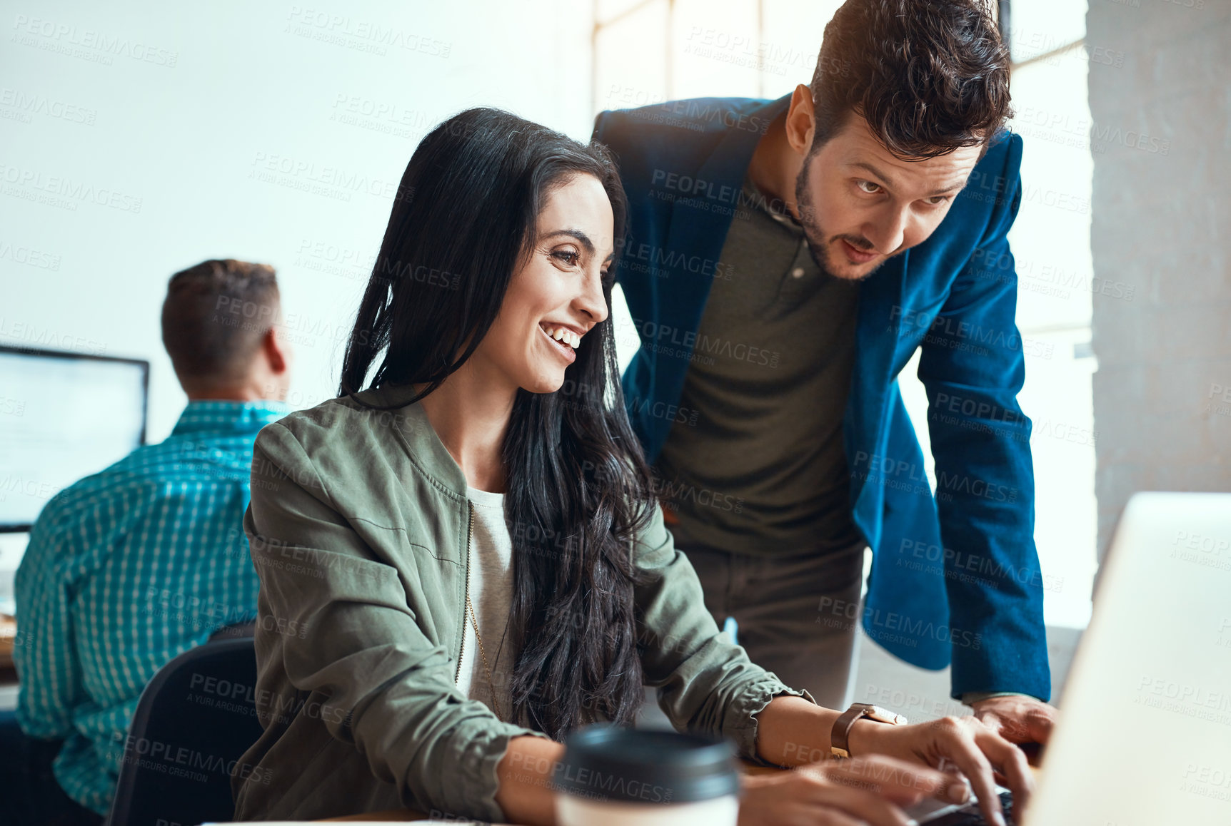 Buy stock photo Shot of two young business colleagues working together in their modern office with a male colleague in the background