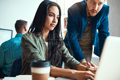 Buy stock photo Shot of two young business colleagues working together in a modern office with their colleagues in the background