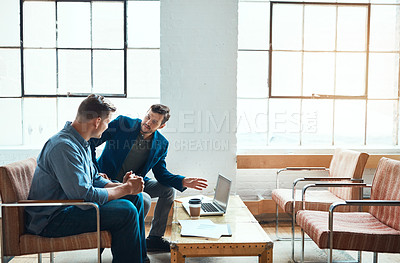 Buy stock photo Shot of two young businessmen having a discussion and using a laptop together in a modern office