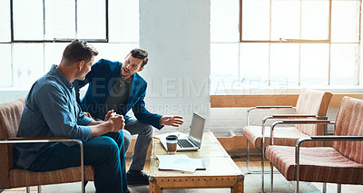 Buy stock photo Shot of two young businessmen having a discussion and using a laptop together in a modern office