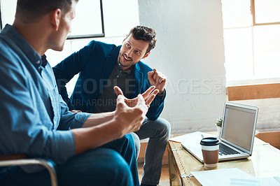 Buy stock photo Shot of two young businessmen having a discussion and using a laptop together in a modern office