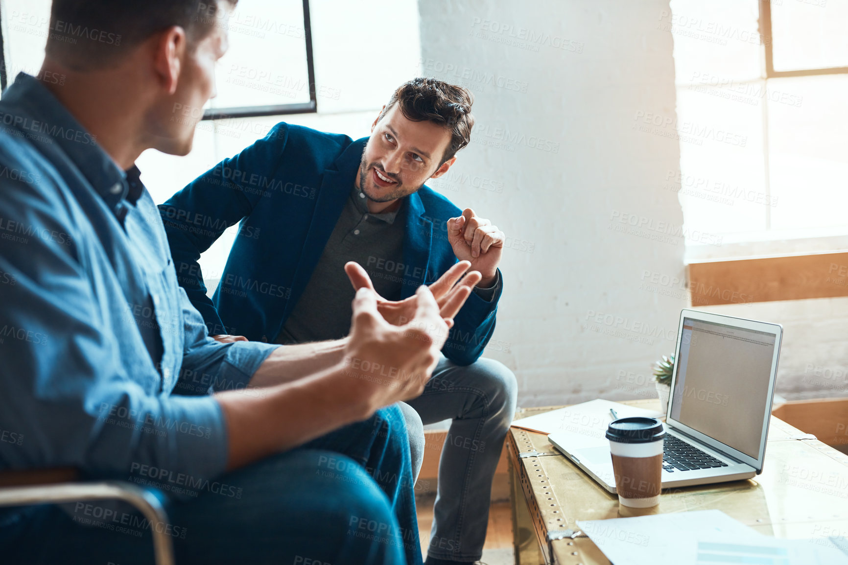 Buy stock photo Shot of two young businessmen having a discussion and using a laptop together in a modern office