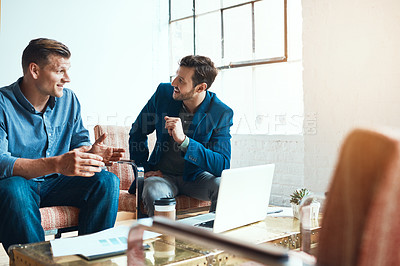 Buy stock photo Shot of two young businessmen having a discussion and using a laptop together in a modern office