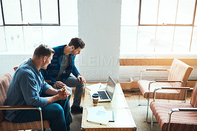 Buy stock photo Shot of two young businessmen having a discussion and using a laptop together in a modern office