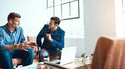 Buy stock photo Shot of two young businessmen having a discussion and using a laptop together in a modern office