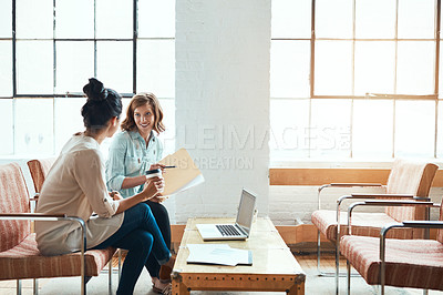 Buy stock photo Shot of two young businesswomen discussing paperwork in a modern office