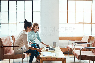 Buy stock photo Shot of two young businesswomen having a discussion and using a laptop together in a modern office