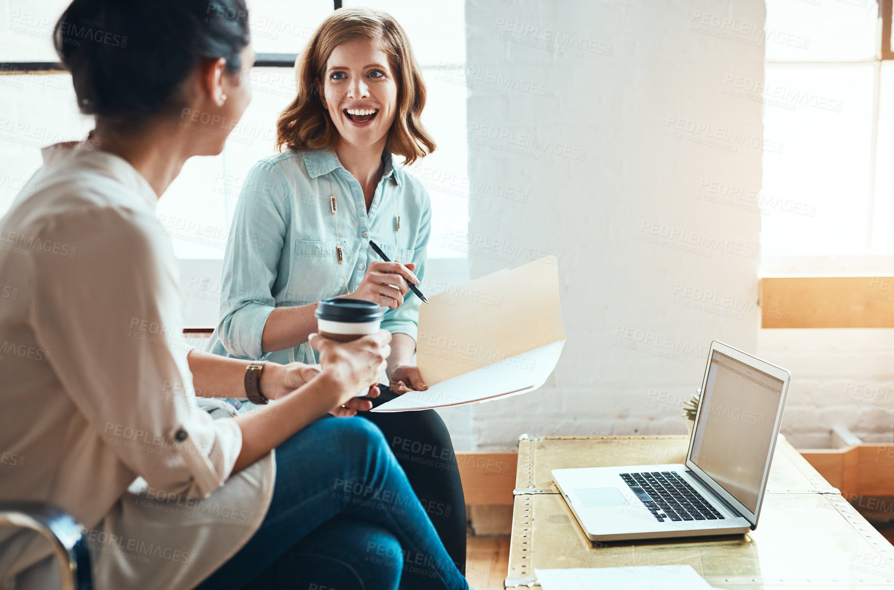 Buy stock photo Shot of two young businesswomen discussing paperwork in a modern office