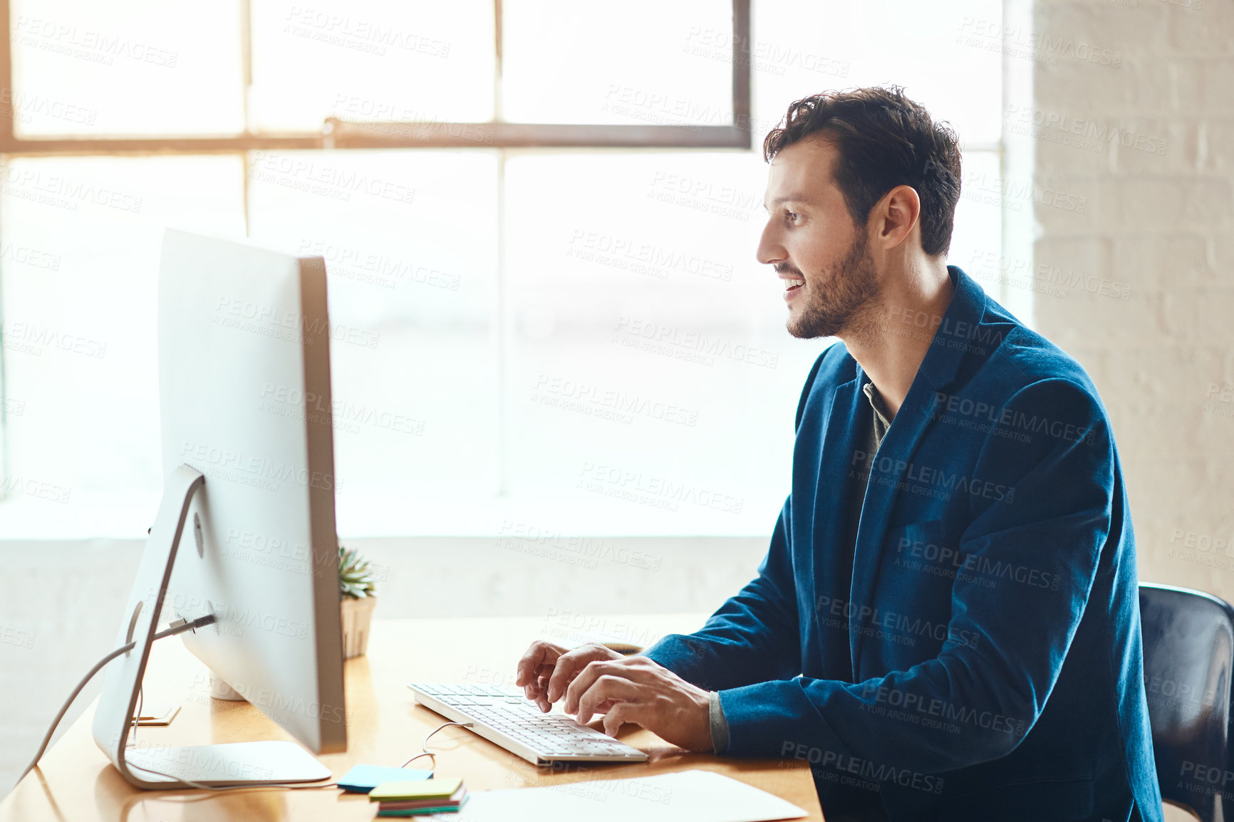 Buy stock photo Cropped shot of a handsome young businessman working on his computer in a modern office