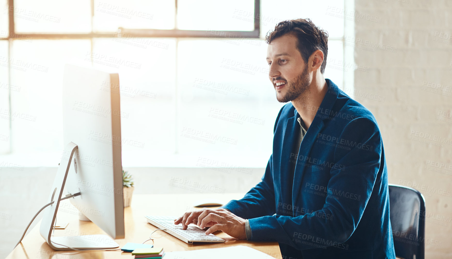 Buy stock photo Cropped shot of a handsome young businessman working on his computer in a modern office