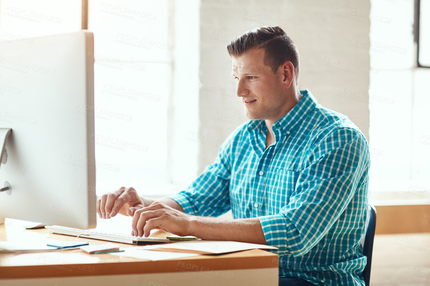 Buy stock photo Cropped shot of a handsome young businessman working on his computer in a modern office