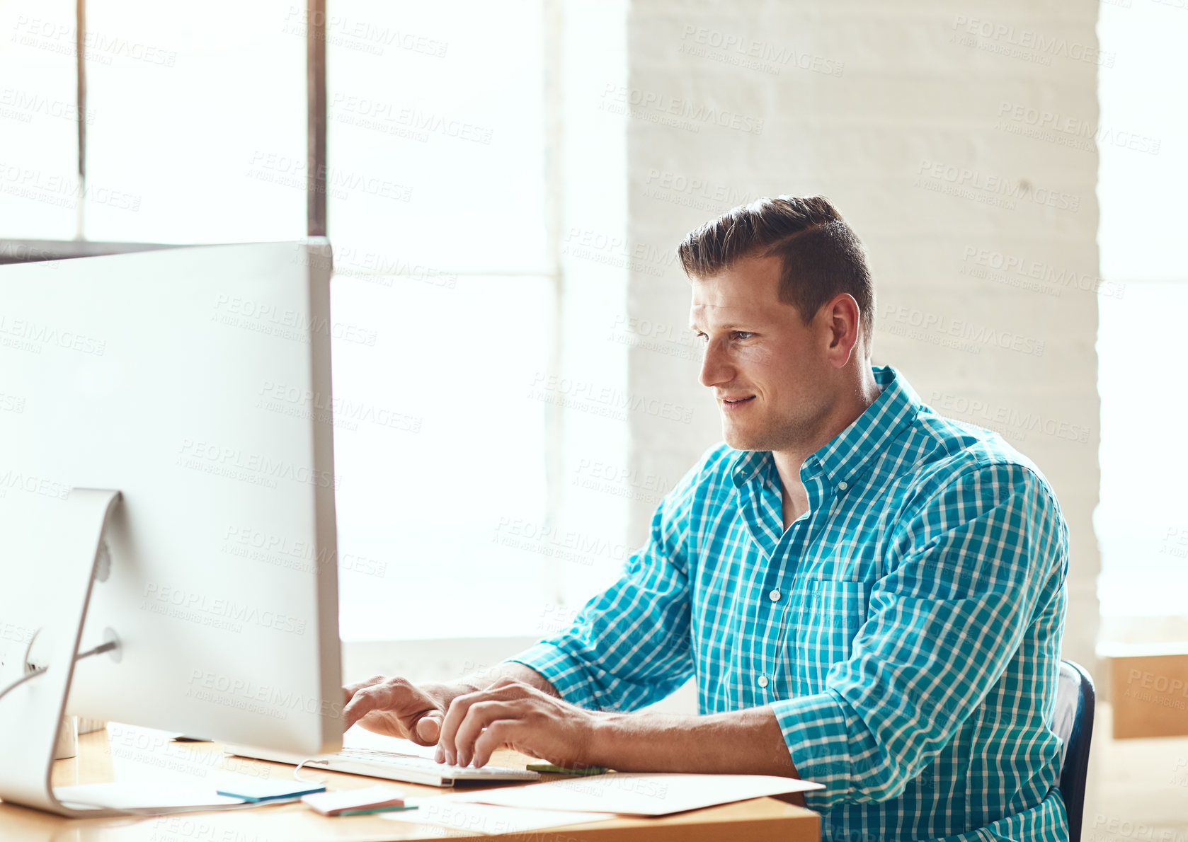 Buy stock photo Cropped shot of a handsome young businessman working on his computer in a modern office