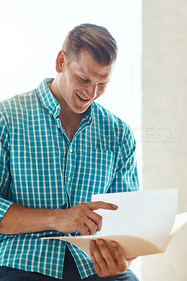 Buy stock photo Cropped shot of a handsome young businessman looking over some paperwork in a modern office