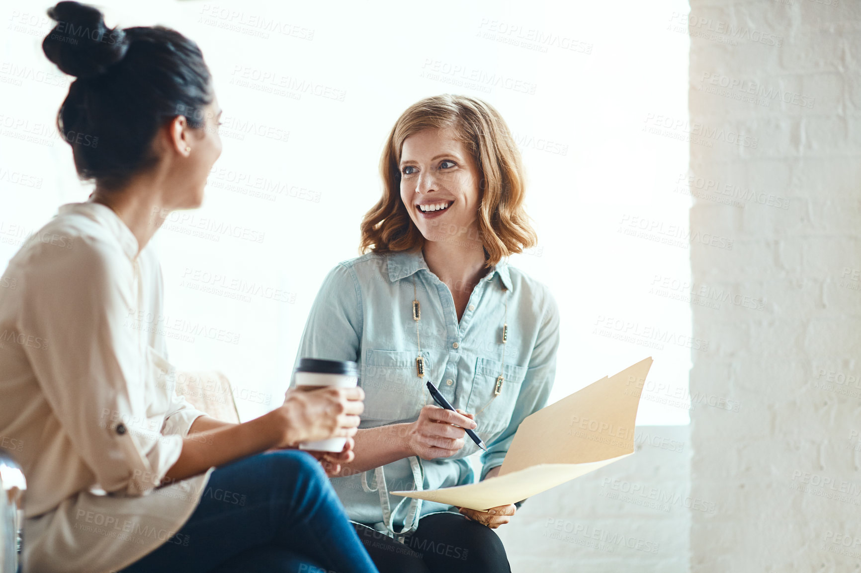 Buy stock photo Cropped shot of two young businesswomen looking over some paperwork together in their modern office