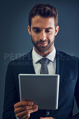 Buy stock photo Studio shot of a handsome young businessman using a digital tablet against a dark background