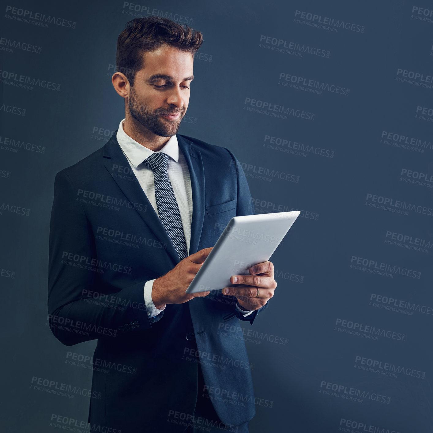 Buy stock photo Studio shot of a handsome young businessman using a digital tablet against a dark background
